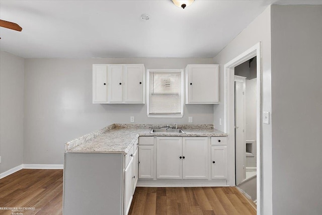 kitchen with light stone counters, baseboards, a sink, dark wood-type flooring, and white cabinetry