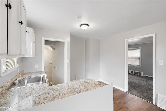 kitchen featuring visible vents, a peninsula, white cabinetry, and a sink