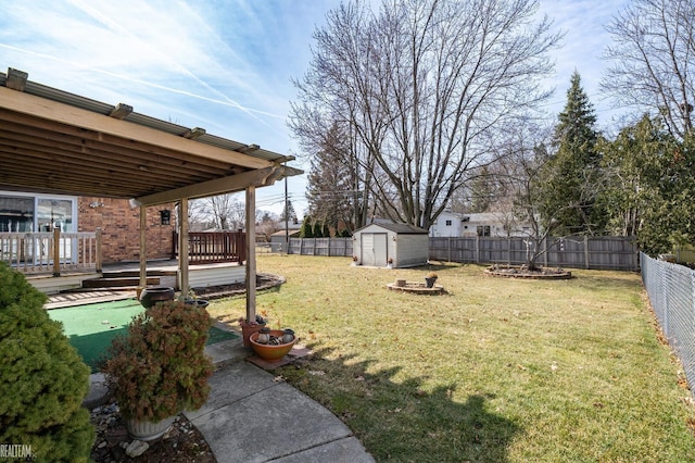 view of yard with an outbuilding, a wooden deck, a storage unit, and a fenced backyard