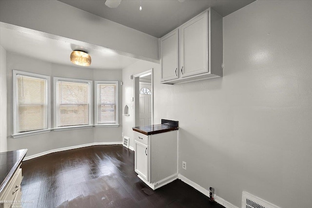 kitchen featuring dark countertops, visible vents, baseboards, dark wood-style floors, and white cabinets