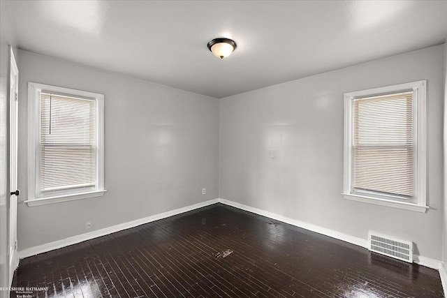 spare room with visible vents, plenty of natural light, baseboards, and dark wood-style flooring