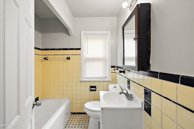 bathroom with a wainscoted wall, a washtub, toilet, vanity, and tile walls