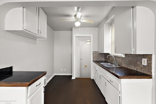 kitchen with a sink, dark countertops, white cabinets, decorative backsplash, and ceiling fan