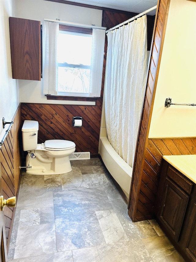 full bath with wooden walls, visible vents, shower / tub combo, wainscoting, and toilet