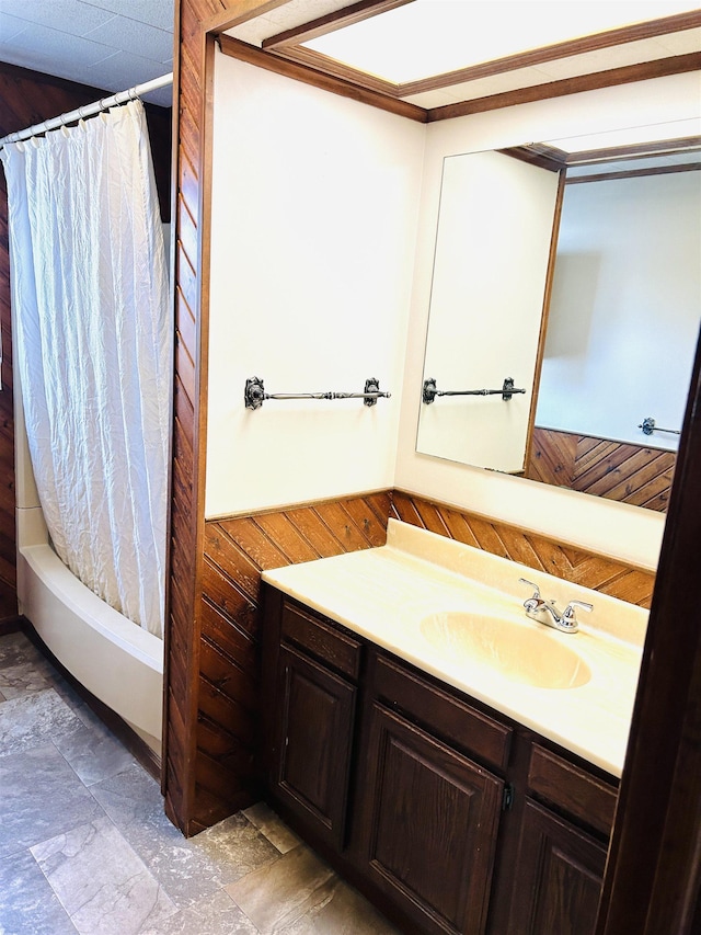 full bath featuring vanity, stone finish floor, wooden walls, and shower / bath combo with shower curtain