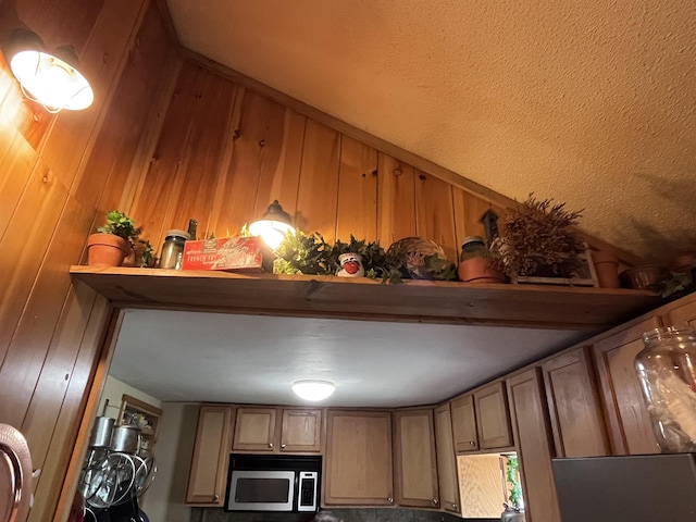 room details featuring stainless steel microwave, brown cabinets, and wood walls