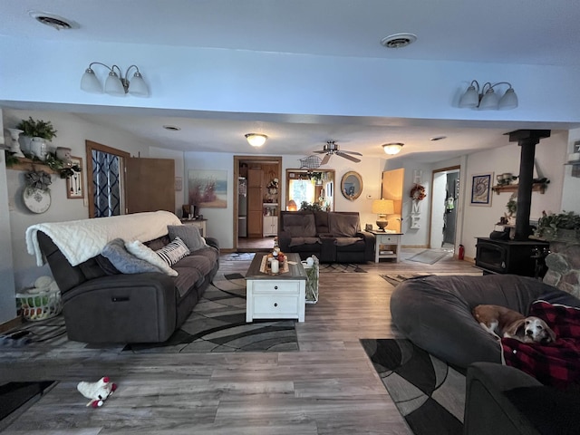 living room with visible vents, a wood stove, ceiling fan, and wood finished floors