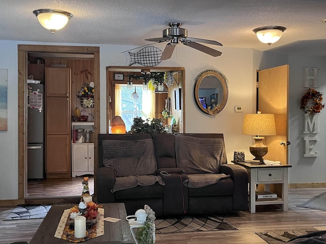 living area featuring baseboards, a textured ceiling, a ceiling fan, and wood finished floors