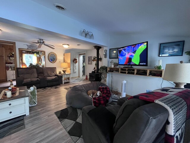 living area featuring visible vents, a wood stove, ceiling fan, and wood finished floors