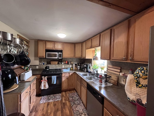 kitchen with dark countertops, tasteful backsplash, appliances with stainless steel finishes, light wood-style floors, and a sink