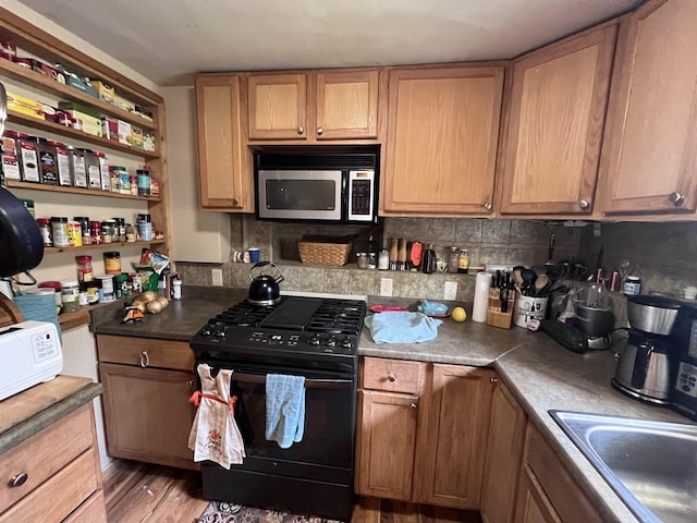 kitchen featuring light wood-style flooring, a sink, black gas range, stainless steel microwave, and tasteful backsplash