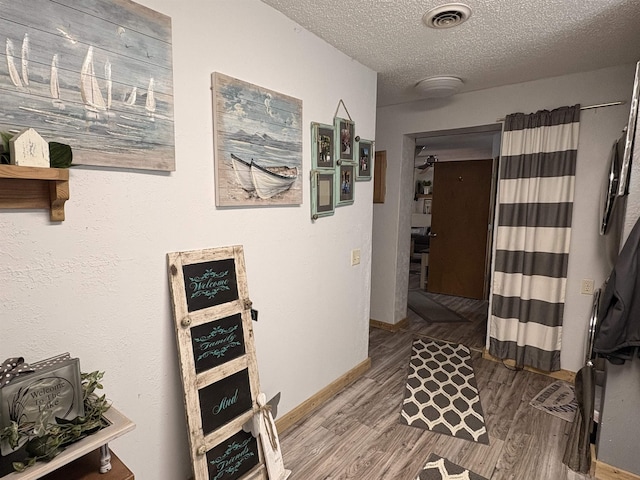 hall with baseboards, wood finished floors, visible vents, and a textured ceiling