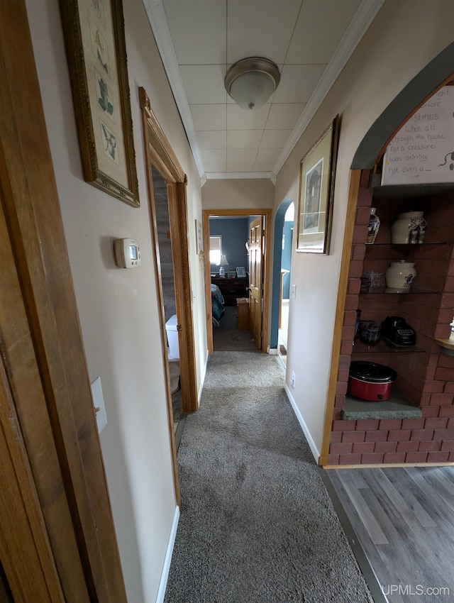 corridor with arched walkways, carpet flooring, crown molding, and baseboards