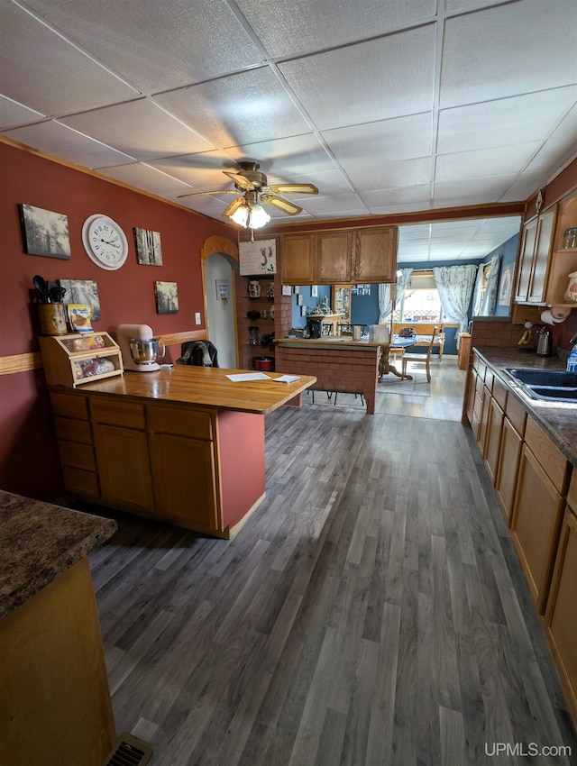 kitchen featuring dark wood-style floors, a peninsula, arched walkways, a drop ceiling, and a sink