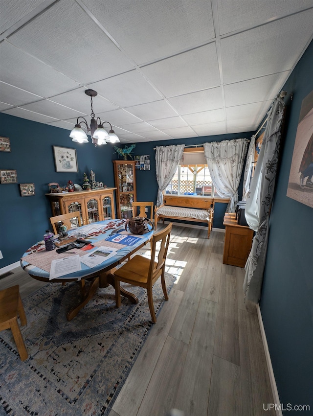 dining space featuring a drop ceiling, baseboards, a notable chandelier, and light wood finished floors