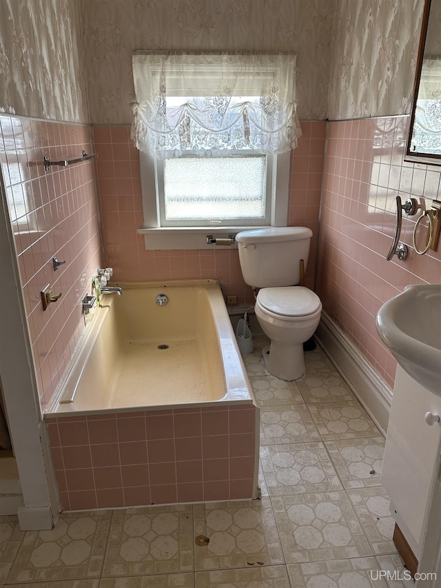 full bath featuring toilet, wallpapered walls, tile walls, and a garden tub