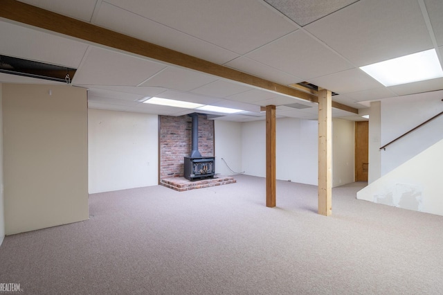 finished basement featuring carpet, a wood stove, and a paneled ceiling