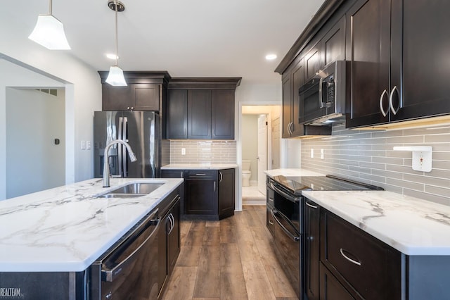 kitchen with light stone countertops, an island with sink, a sink, dark wood-type flooring, and appliances with stainless steel finishes