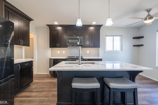 kitchen featuring stainless steel microwave, dark wood finished floors, freestanding refrigerator, a breakfast bar area, and ceiling fan