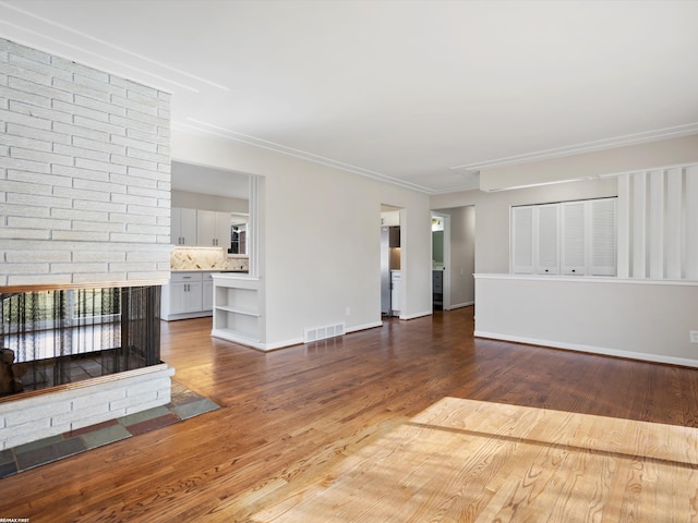 unfurnished living room featuring visible vents, a brick fireplace, crown molding, baseboards, and wood finished floors