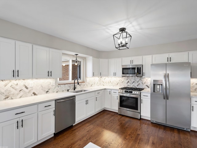 kitchen featuring dark wood-type flooring, appliances with stainless steel finishes, a notable chandelier, white cabinetry, and a sink