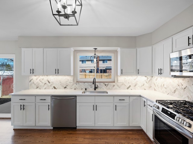 kitchen with dark wood-type flooring, a sink, appliances with stainless steel finishes, white cabinets, and a chandelier