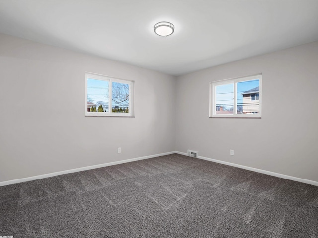 unfurnished room with visible vents, baseboards, dark colored carpet, and a wealth of natural light