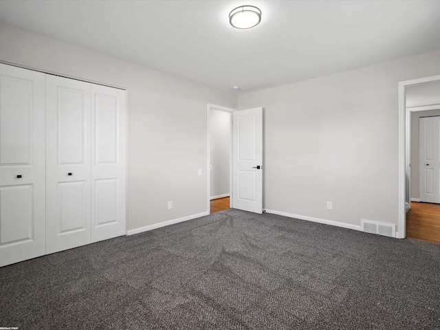 unfurnished bedroom with dark colored carpet, visible vents, baseboards, and a closet