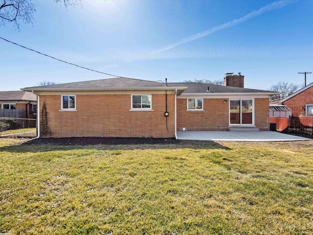 back of house featuring fence, brick siding, a lawn, and a patio area