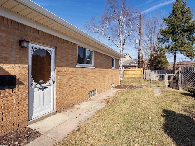 view of exterior entry with fence, brick siding, and a lawn