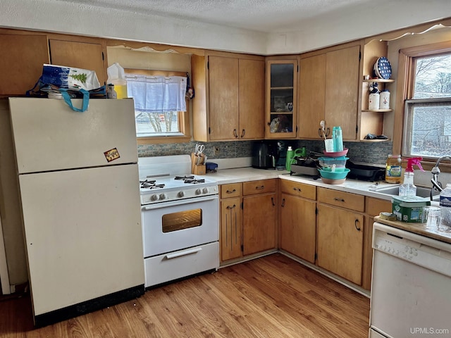 kitchen with light wood-type flooring, white appliances, brown cabinetry, light countertops, and decorative backsplash