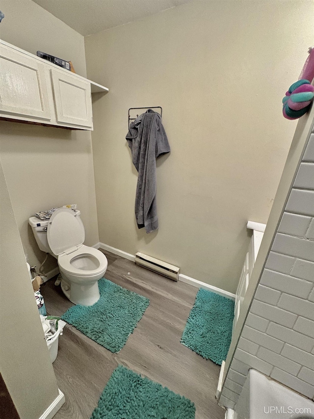 bathroom with a baseboard heating unit, toilet, wood finished floors, and baseboards