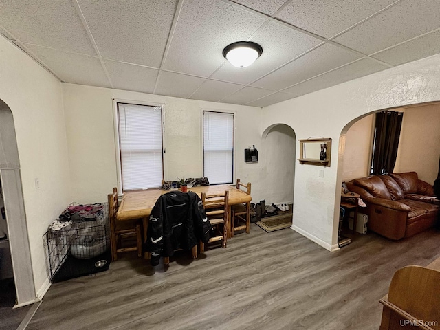 office area with baseboards, wood finished floors, arched walkways, and a paneled ceiling