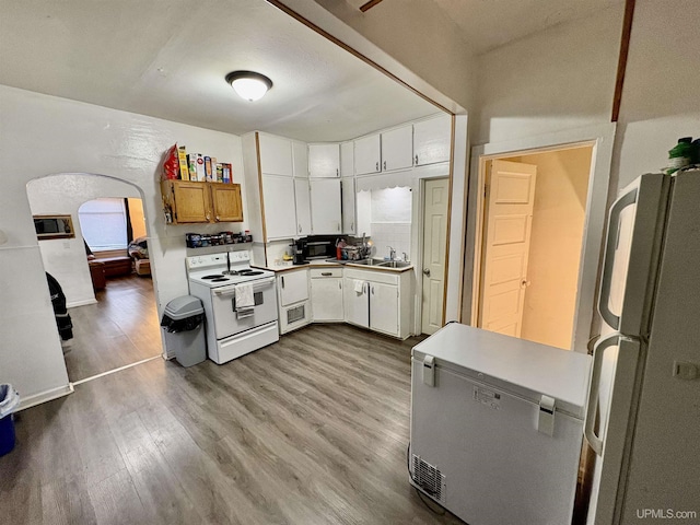 kitchen featuring white appliances, wood finished floors, light countertops, and a sink