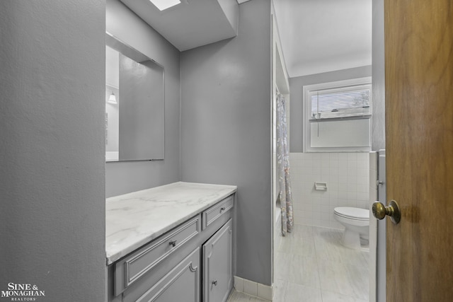 full bath with shower / bath combo with shower curtain, toilet, tile walls, and vanity