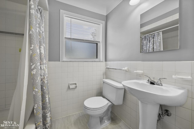 full bath featuring a shower with curtain, tile walls, toilet, and a wainscoted wall