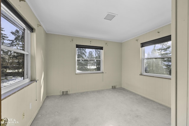 spare room featuring a wealth of natural light, visible vents, light colored carpet, and crown molding