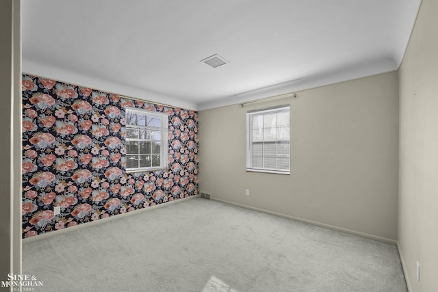 spare room with wallpapered walls, carpet flooring, visible vents, and baseboards