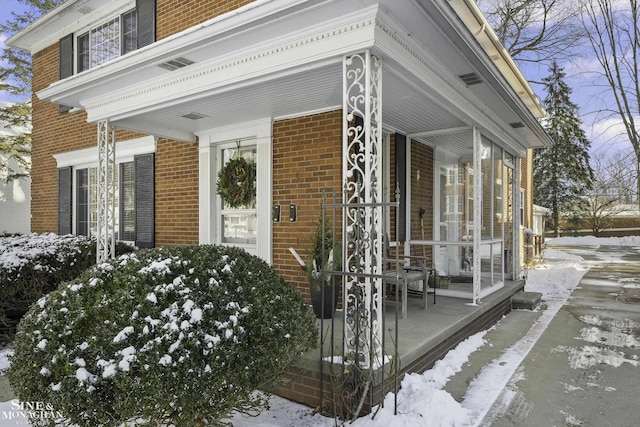 snow covered property entrance with brick siding and covered porch