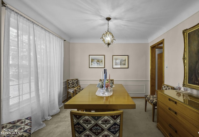 carpeted dining space with a decorative wall, wainscoting, and an inviting chandelier