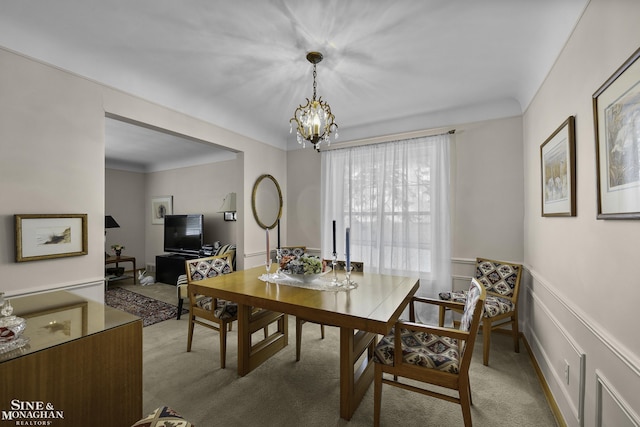 carpeted dining space featuring an inviting chandelier, a decorative wall, and wainscoting