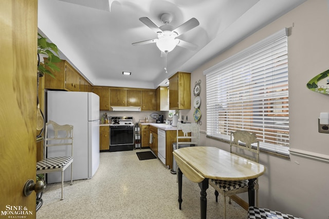 kitchen with brown cabinets, under cabinet range hood, white appliances, light countertops, and ceiling fan