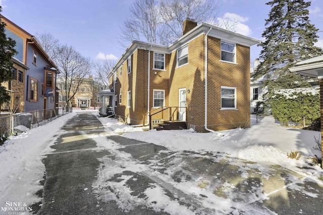 snow covered property with brick siding and a chimney