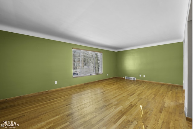 empty room featuring visible vents, light wood-type flooring, and baseboards