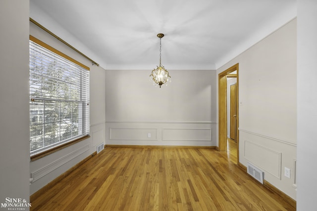 spare room featuring wainscoting, light wood-style floors, visible vents, and a chandelier