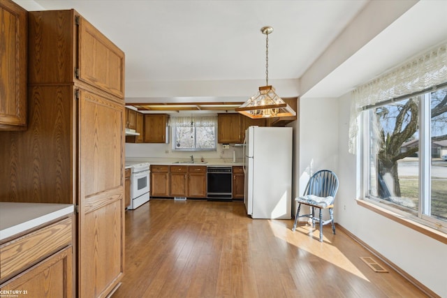 kitchen featuring visible vents, a sink, under cabinet range hood, hardwood / wood-style floors, and white appliances