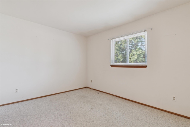 spare room featuring light carpet and baseboards