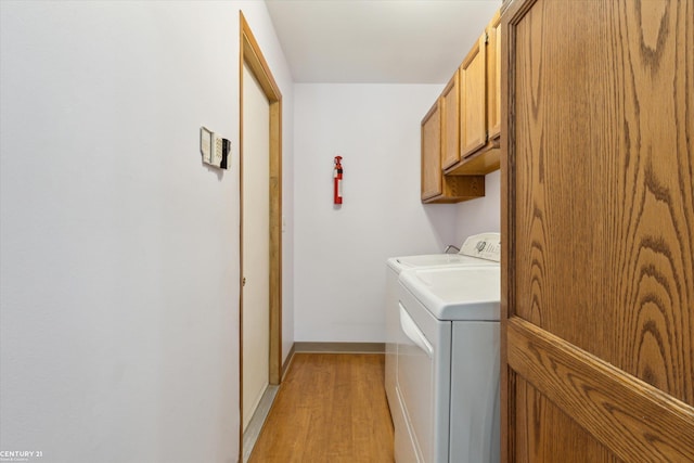 clothes washing area with washing machine and dryer, cabinet space, baseboards, and light wood-style floors