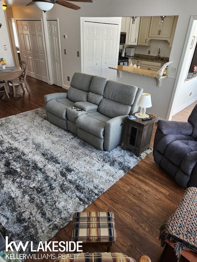 living room with baseboards, a ceiling fan, and dark wood-style flooring