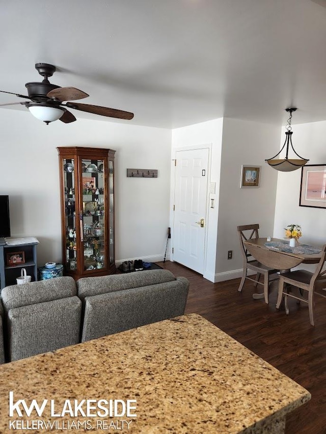 living room featuring baseboards, a ceiling fan, and dark wood-style flooring